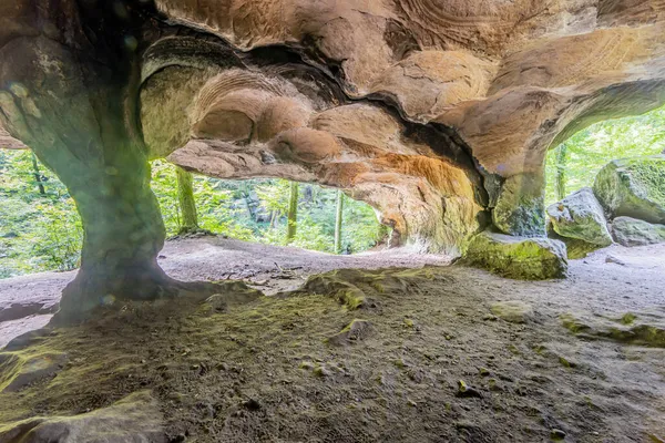 Güneş ışığı Huel Lee veya Hohllay kaya oluşumunun eski taş ocağına, oyuk taşa mağara tavanında dairesel desenlere, arka planda yeşil ağaçlara, Lüksemburg 'da Mullerthal Trail' e yansıyor.