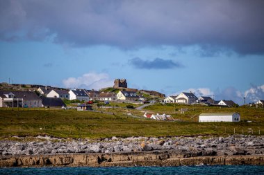 Beautiful view of the Inis Oirr island with its houses and the ruined 15th-century castle tower in a prehistoric stone fort in the background, wonderful sunny day in Aran Islands, Ireland clipart