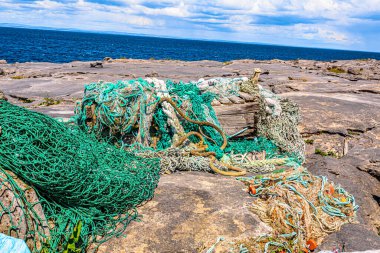 Accumulation of marine litter, such as fishing nets, ropes, wood with the sea in the background on the rocky coastal beach of the island of Inis Oirr, sunny day in Inisheer island, Ireland