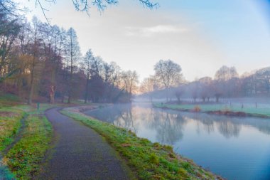River with reflection in the water in the middle of a nature reserve with a pedestrian path, beautiful misty sunrise in Elsloo, South Limburg in the Netherlands Holland