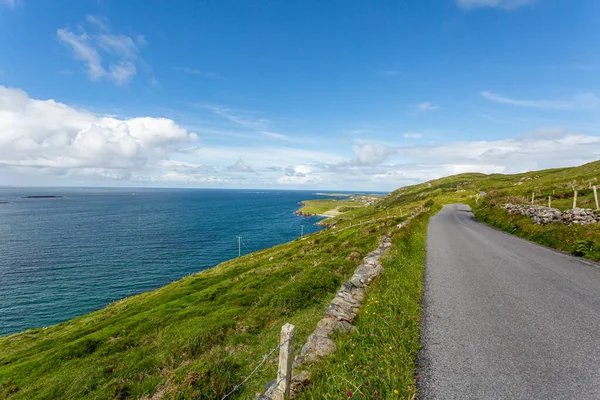 Sky Road with the most spectacular panoramic views of the Atlantic Ocean and Connemara coastline, paved path between green grass and rocks, sunny spring day in Clifden, County Galway, Ireland