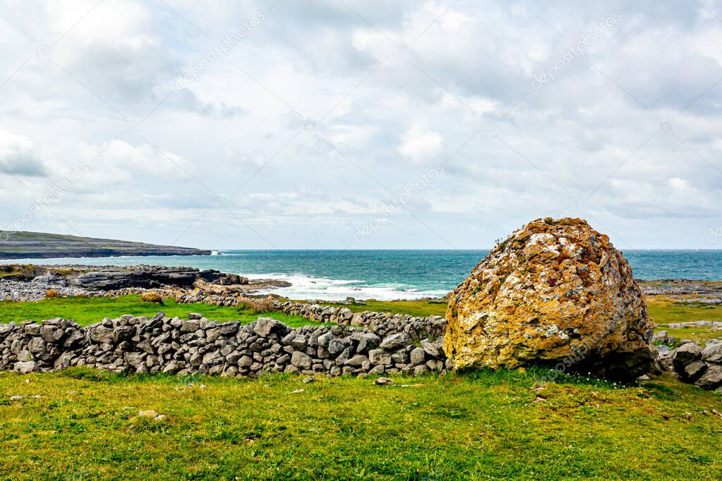 Irish landscape of a giant stone next to a stone fence with the sea in the background between Bothar nA hAillite and Fanore, Wild Atlantic Way, wonderful spring day in County Clare in Ireland