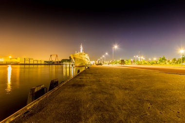 Night view of the port of Rotterdam with a cruise ship anchored on the quay, empty street with illuminated lamp posts and trees in the background, quiet night with a clear sky in the Netherlands