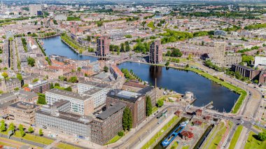 Aerial cityscape of Rotterdam with its buildings, canal, bridges, boats and small green areas, sunny day with a grayish sky with the horizon in the background in South Holland, Netherlands
