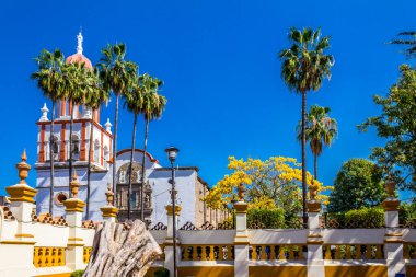 Facade of the church of San Pedro Apostol surrounded by a white wall with yellow details and palm trees, wonderful and sunny day in Tlaquepaque Jalisco Mexico