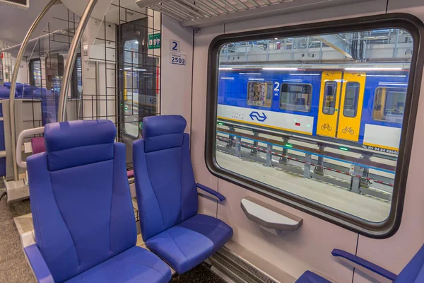 Maastricht, South Limburg / Netherlands, September 30, 2017. Blue chairs next to a window inside, seeing through the window a local train in the new workshop of the Dutch company Nedtrain (NS)