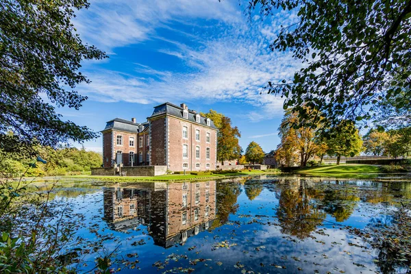 Voerendaal, South limburg / Netherlands. October 14th, 2018. Cortenbach Castle with its pond with mirror reflection and dry leaves on the water surrounded by trees, sunny autumn day with a blue sky