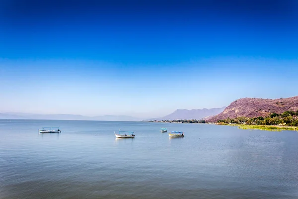 Boats anchored on the calm waters of Lake Chapala with mountains in the background blurred and misty, sunny day with a blue sky in the state of Jalisco Mexico