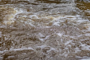 Nehrin suları, dalgaları oluşturan ve köpüğe neden olan türbülanslar, geri kalanı bulanık ve arka plan bulanık.