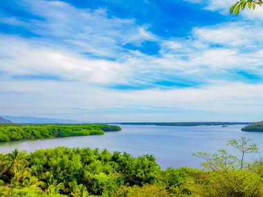 Yeşil bitki örtüsüyle çevrili sakin sularıyla Cuyutlan Gölü, arka planda bol beyaz bulutlu mavi gökyüzü, Manzanillo, Colima Mexico 'da tropikal bahar günü