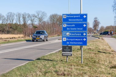 Someren, Kuzey Brabant, Hollanda. 27 Şubat 2022. Araba yolda giderken, doğa koruma alanı Vennenhorst gibi farklı istikametleri gösteren işaretler, arka planda çıplak ağaçlar