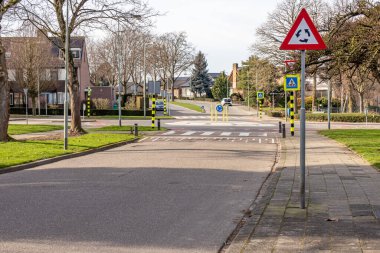 Kavşak, yaya geçidi, kırmızı, siyah, beyaz ve oklarla üçgen plakalı metal direkli kavşak ve bulanık arka planda ev için üçgen trafik levhası.