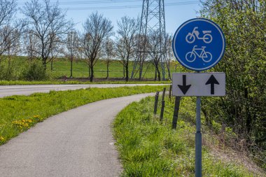 Cycle lane in both directions along a country road, sign indicating: lane for bicycles and mopeds, bare trees in the blurred background, sunny day in Stevensweert, South Limburg, the Netherlands