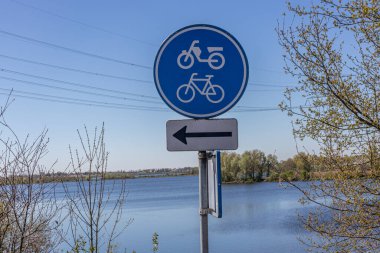 Trafik levhası gösteriyor ki: siyah oklu bisiklet ve motosikletler için şerit, mavi ve beyaz yuvarlak plaka, Hollanda 'da arka planda bir nehrin suyu