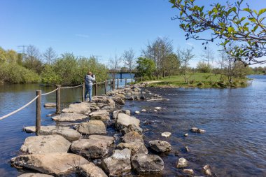 Oude Maas nehri üzerindeki Brug Molenplas 'da basamak taşları, fotoğraf çeken bir erkek turistin dikiz görüntüsü, arka planda yeşil ağaçlar, Stevensweert, Güney Limburg, Hollanda' da güneşli bir gün.
