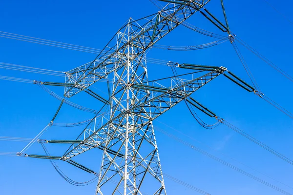 Devasa yüksek voltajlı bir elektrik kulesinin tepesine yakın plan olarak açık mavi gökyüzü ve düşük perspektiften bakıldığında güneşli bir gün.