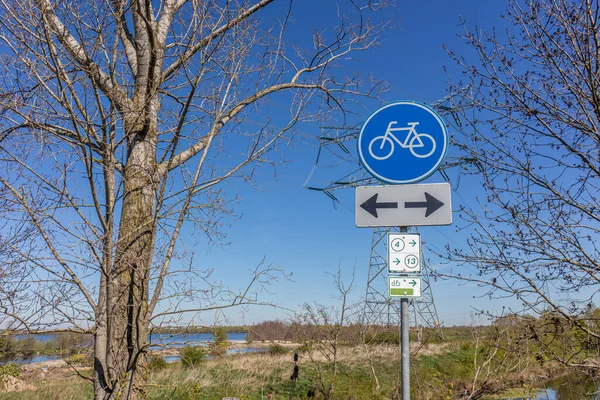 Traffic sign: cycle lane in both directions, blue and white round plate, cycle routes 4 and 13, Oude Maas river and Molenplas nature reserve in the background, Stevensweert, South Limburg, Netherlands