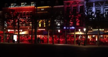 Maastricht, South Limburg, Netherlands. March 8, 2022. Illuminated restaurant terraces with red, yellow and blue lights at Vrijthof. People walking leisurely, bikes parked on a corner, quiet night