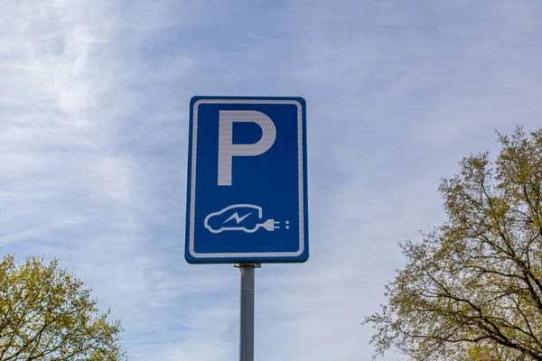 Parking sign and charging station for electric cars, blue plate with a P and a drawing of a car with an electric plug, blue sky with few clouds in the background. Clean green energy concept