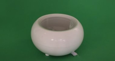 Close-up of pouring water into a white aroma oil diffuser humidifier, against a green studio background. Concept of ambient relaxation at home