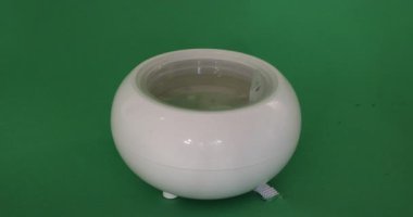 Close-up of placing the plastic caps on a white aroma oil diffuser humidifier, against a green studio background. Concept of ambient relaxation at home