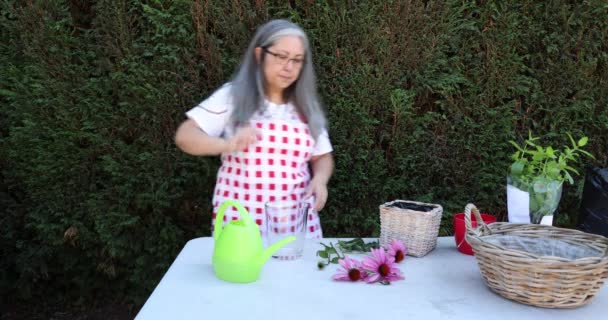 Mature Woman Pouring Water Glass Vase Placing Three Purple Flowers — Stockvideo