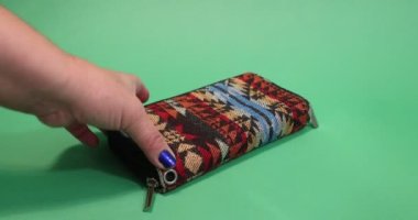 Adult female hands opening a multicolored fabric purse and realizing it is empty against a green studio background. Concept of poverty in inflation time