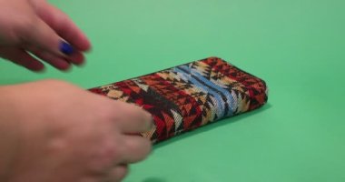 Adult female hands opening a multi-colored fabric purse with 100 and 50 euro bills, closing it and placing it on a surface against a green studio background. Concept of economy and prosperity