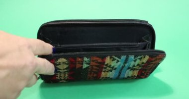 Adult female hands placing 100, 50, 10 and 5 euro bills into a multicolored fabric purse against a green studio background. Concept of economy, financial planning and prosperity
