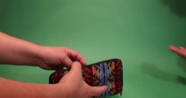 Adult female hands taking 100 euro notes out of her purse to pay and male hands taking them and indicating that it is two more against a green studio background. Economy and prosperity concept