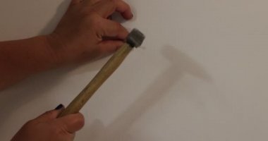 Yetişkin kadın elleri beyaz bir duvara çivi çakıyor, parmaklarıyla tutuyor, çekiçle vuruyor, çivi çakıyor. Tadilat ve dekorasyon kavramı