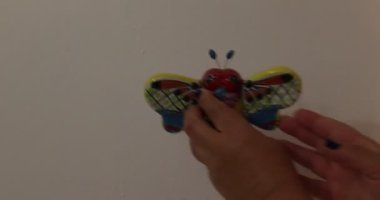 Adult female hands hanging a talavera bee against a white wall, yellow, orange, green and brown colors. Original concept of decoration for the home