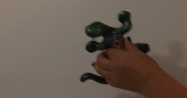 Adult female hands placing a green salamander decorated with yellow and orange flowers against a white wall on a terrace. Original concept of decoration for the home