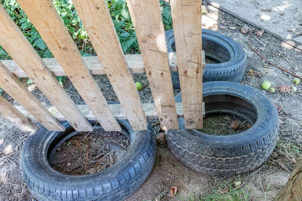 Three car tires dumped and abandoned under some wooden planks in the backyard of a farm against ground, sparse green vegetation in background, sunny summer day. Concept of environmental pollution