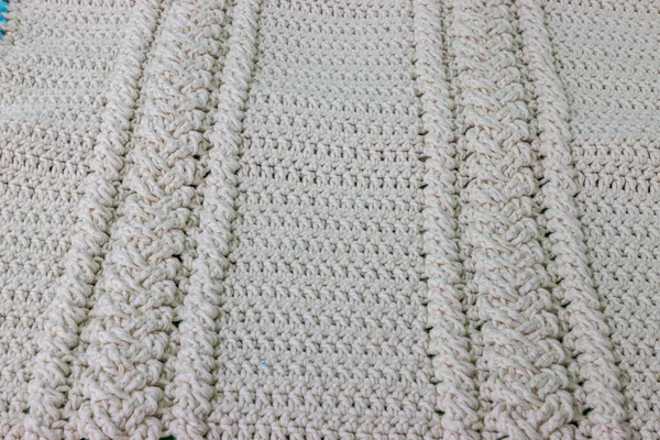 Top view of the surface of a crochet blanket finished in beige cotton yarn, two intertwined braids, original embossed crochet stitch pattern. Handmade craft creativity