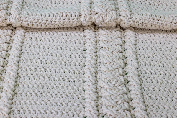 Top view of a crochet blanket in beige cotton yarn folded at the top, two braids intertwined, original embossed crochet stitch pattern. Handmade craft creativity