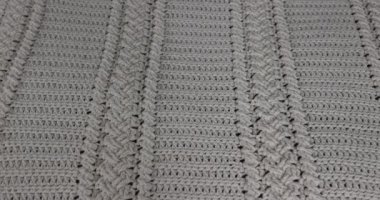 Surface of a crochet blanket with intertwined braids finished in beige cotton thread, over putting another white blanket on top, embossed stitch pattern. Handmade craft creativity