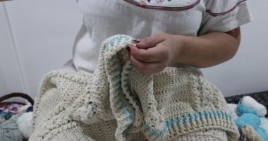 Senior adult female hands starting to knit a blanket edge in beige cotton yarn, removing stitch marker, pink metal crochet hook, blue detail, embossed crochet stitch pattern. Handmade craft creativity
