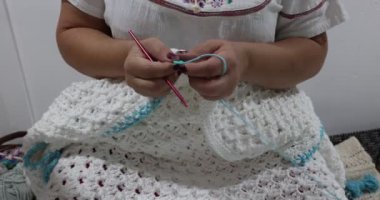 Senior female hands removing green stitch marker and beginning to knit edge in blue cotton yarn on white crochet blanket, pink metal hook, embossed crochet stitch pattern. Handmade craft creativity