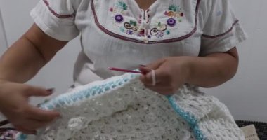 Female adult hands knitting the interlocking blue and white colors border in stretchy pattern of a white crochet blanket, pink metal hook, embossed crochet stitch pattern. Handmade craft creativity