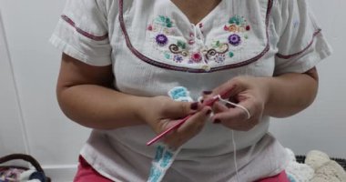 Female adult hands starting to crochet blanket with simple interlocking square pattern in white and blue colors, pink metal hook, original embossed crochet stitch pattern. Handmade craft creativity
