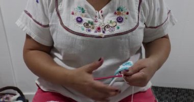 Female adult hands checking the beginning of a crochet blanket with simple interlocking squares pattern in white and blue colors, pink metal hook, embossed stitch pattern. Handmade craft creativity