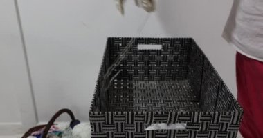 Adult female hands placing two unfinished crochet blankets in a work box, one beige and one white with blue details on the edges, original embossed crochet stitch pattern. Handmade creativity