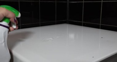 Female hands spraying detergent on the white lid cover of a domestic gas stove. scrubbing with a kitchen sponge, big red plastic gloves. Cleaning and housework concept