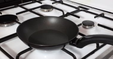 Close-up when olive oil is poured into a pan before starting preparation of a delicious meal, black grates, burners, white cover, black non-stick pan, glass bottle. Concept of delicious homemade food