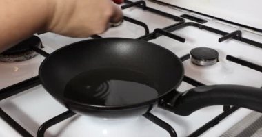 Adult female hands placing two eggs in a pan on a gas stove, fried eggs, full yellow yolk, egg white, oil, fire on, burner, white cover, metal grill. Concept of delicious homemade food