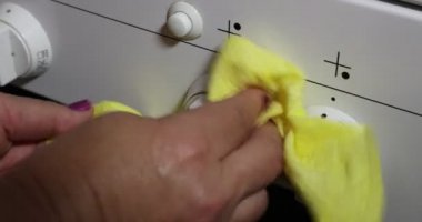 Close-up of adult female hands, cleaning dirty gas stove knobs, using detergent and a yellow rag. Cleaning and housework concept