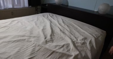 Yetişkin hizmetçi yatağı yapmak için bej pamuklu yatak üstünü sallıyor, hizmetçi servisi. Ev işi kavramı