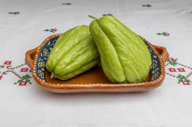 Meksika kil tepsisindeki iki organik chayote kırmızı çiçekleri çapraz dikişli bir masa örtüsü, labu siam, jipang olarak da bilinir. Biyolojik, biyolojik ve doğal yetiştirme kavramı