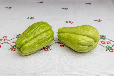 Çapraz dikişli kırmızı çiçekli bir masa örtüsü üzerinde iki organik chayote, labu siam, jipang olarak da bilinir. Biyolojik, biyolojik ve doğal yetiştirme kavramı